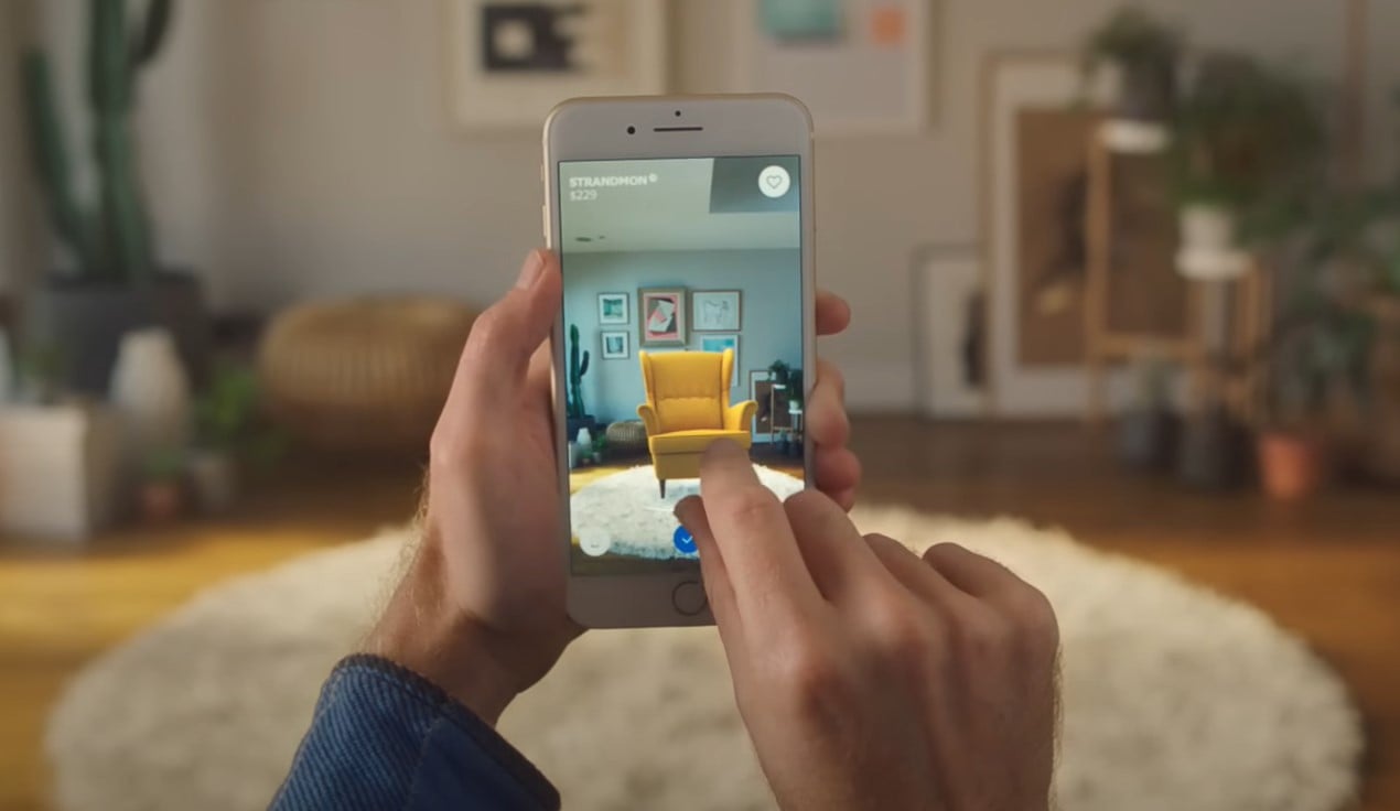 A person using the IKEA Place app on a smartphone to visualize how a yellow armchair would look in their living room